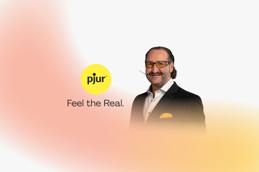 Alexander Giebel, Gründer und CEO von pjur, neben dem gelben pjur-Logo mit dem Slogan „Feel the Real“.
