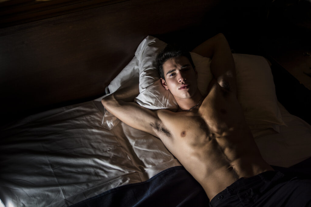 Junger Mann oberkörperfrei im Bett liegend